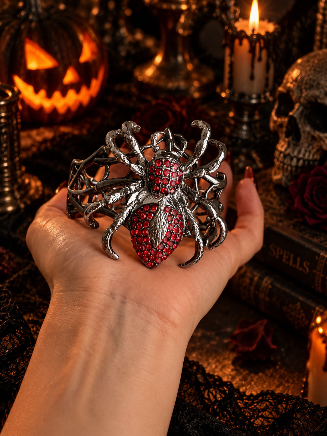 Model hand holding gothic crimson rhinestone spiderweb cuff bracelet in front of Halloween decor