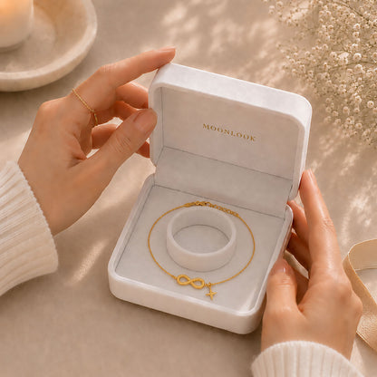 Hands gently opening a white Moonlook gift box containing a delicate gold-tone infinity and star anklet.
