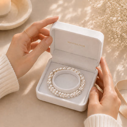 Hands gently opening a white Moonlook gift box revealing a beautiful double-layer pearl bracelet.