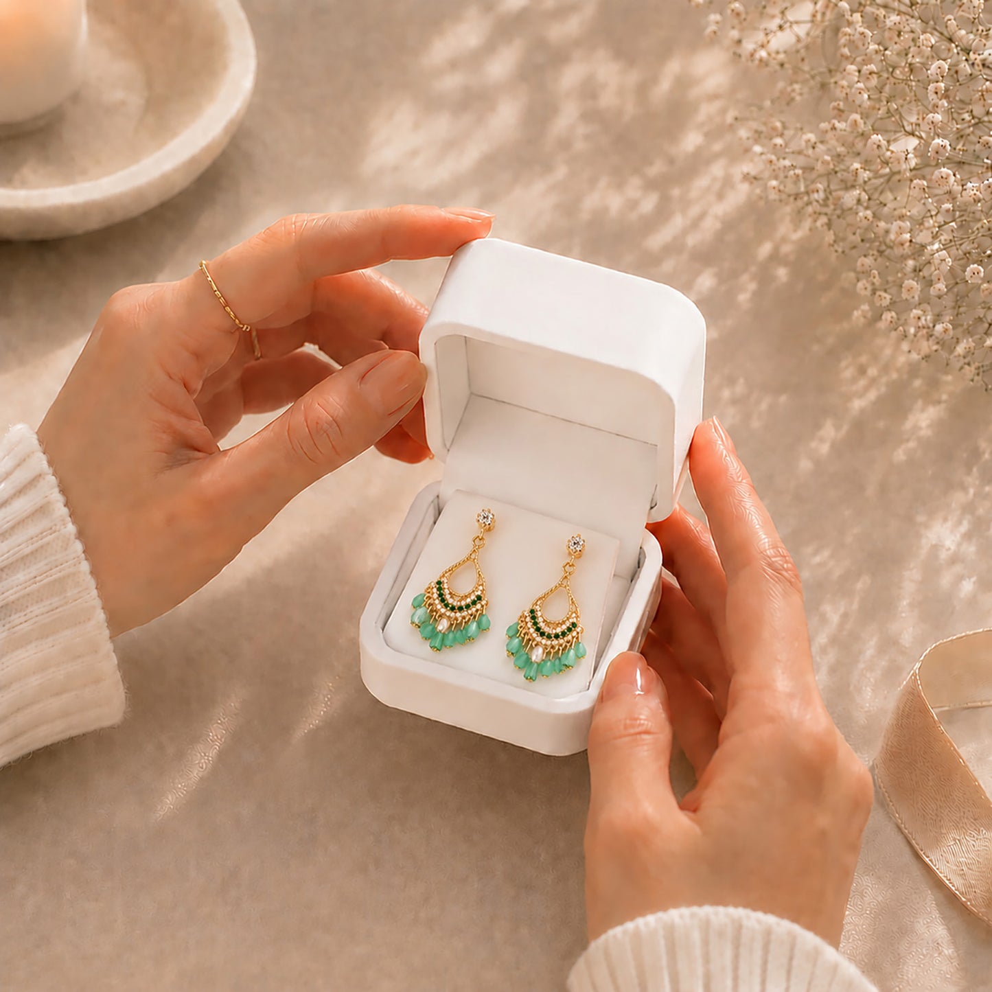 Hands gently opening a premium white Moonlook jewelry box revealing vibrant green bohemian tassel earrings.