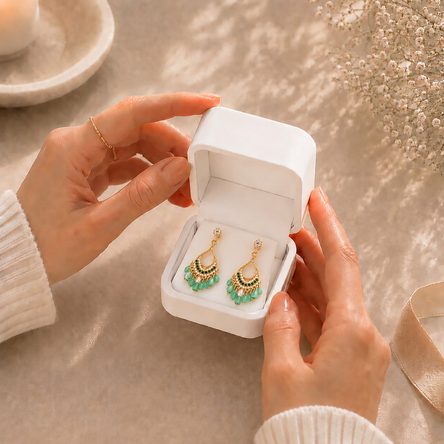 Hands gently opening a premium white Moonlook jewelry box revealing vibrant green bohemian tassel earrings.