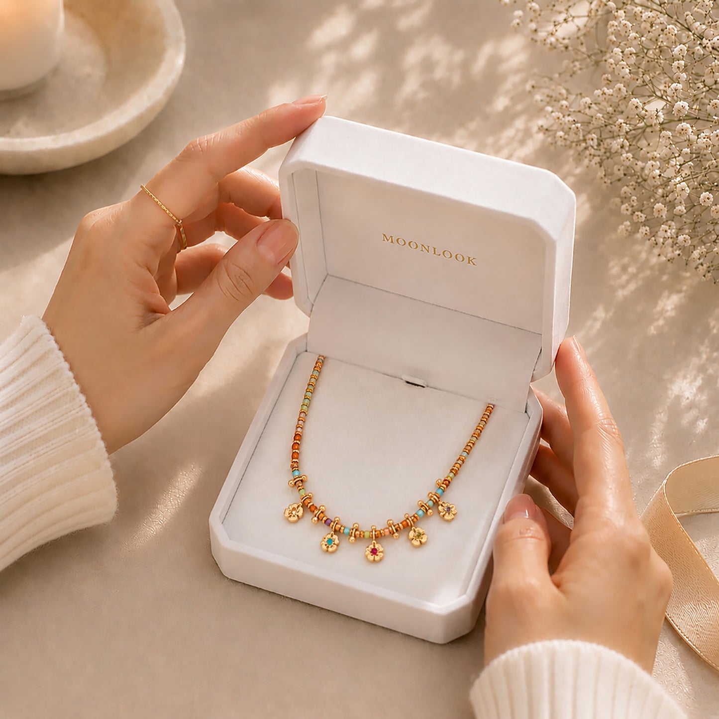 Hands opening a premium white Moonlook jewelry box revealing a vibrant beaded floral necklace.