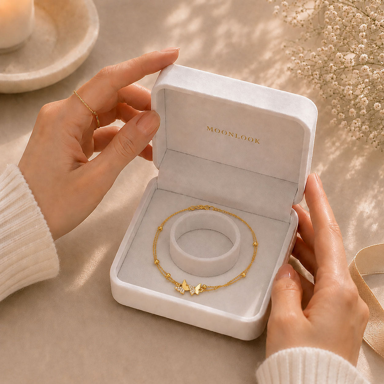 Hands opening a premium white Moonlook jewelry box revealing a delicate gold-tone butterfly anklet.