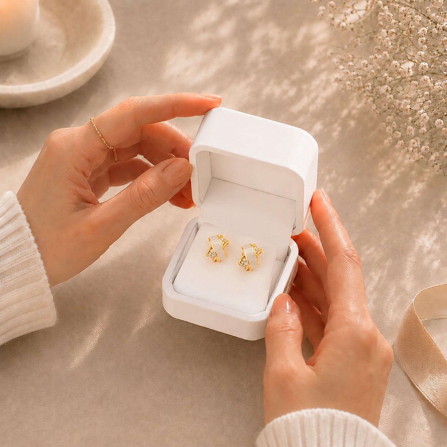 Hands opening a premium white Moonlook jewelry box revealing gold-tone criss-cross stud earrings.