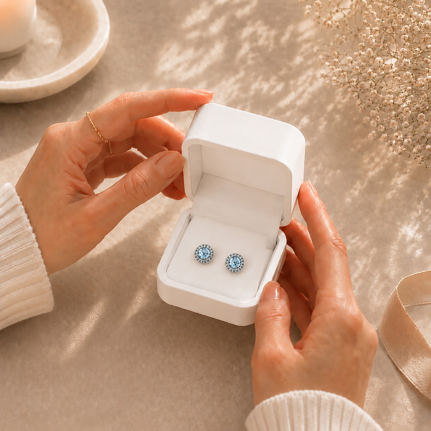 Hands gently opening a premium white Moonlook jewelry box revealing beautiful blue halo stud earrings.