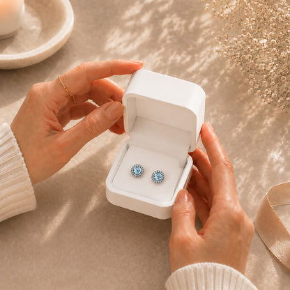 Hands gently opening a premium white Moonlook jewelry box revealing beautiful blue halo stud earrings.