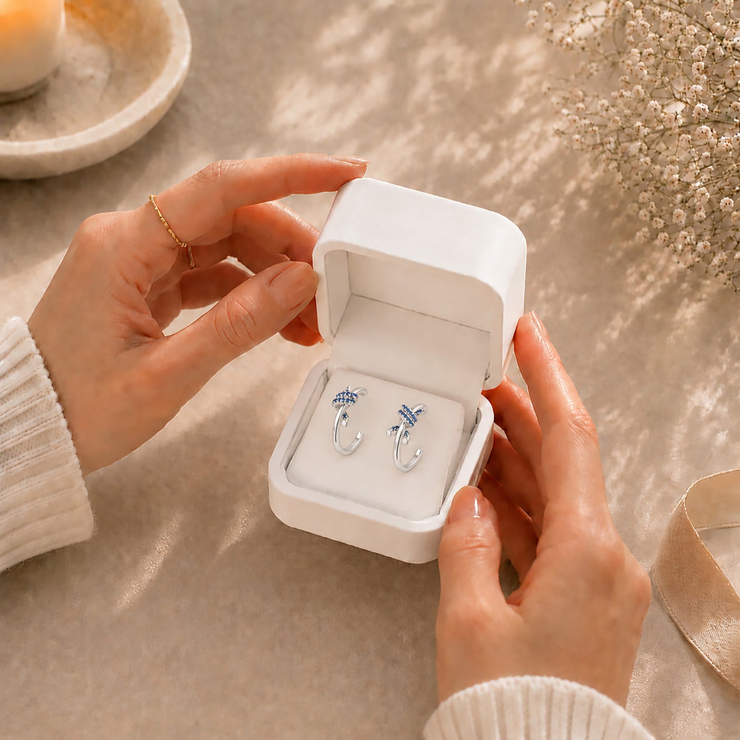 Hands gently opening a premium white Moonlook jewelry box revealing delicate sapphire blue knot earrings.