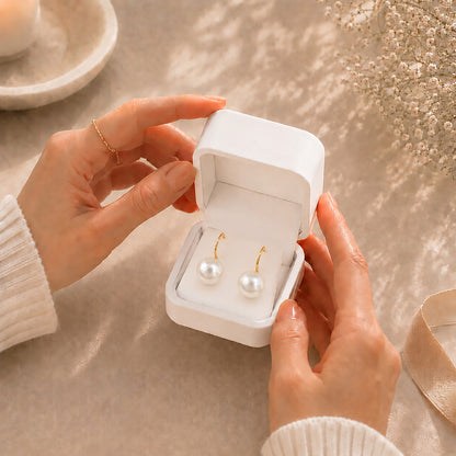 Hands gently opening a premium white Moonlook jewelry box revealing stunning 14K gold-plated oversized pearl earrings.