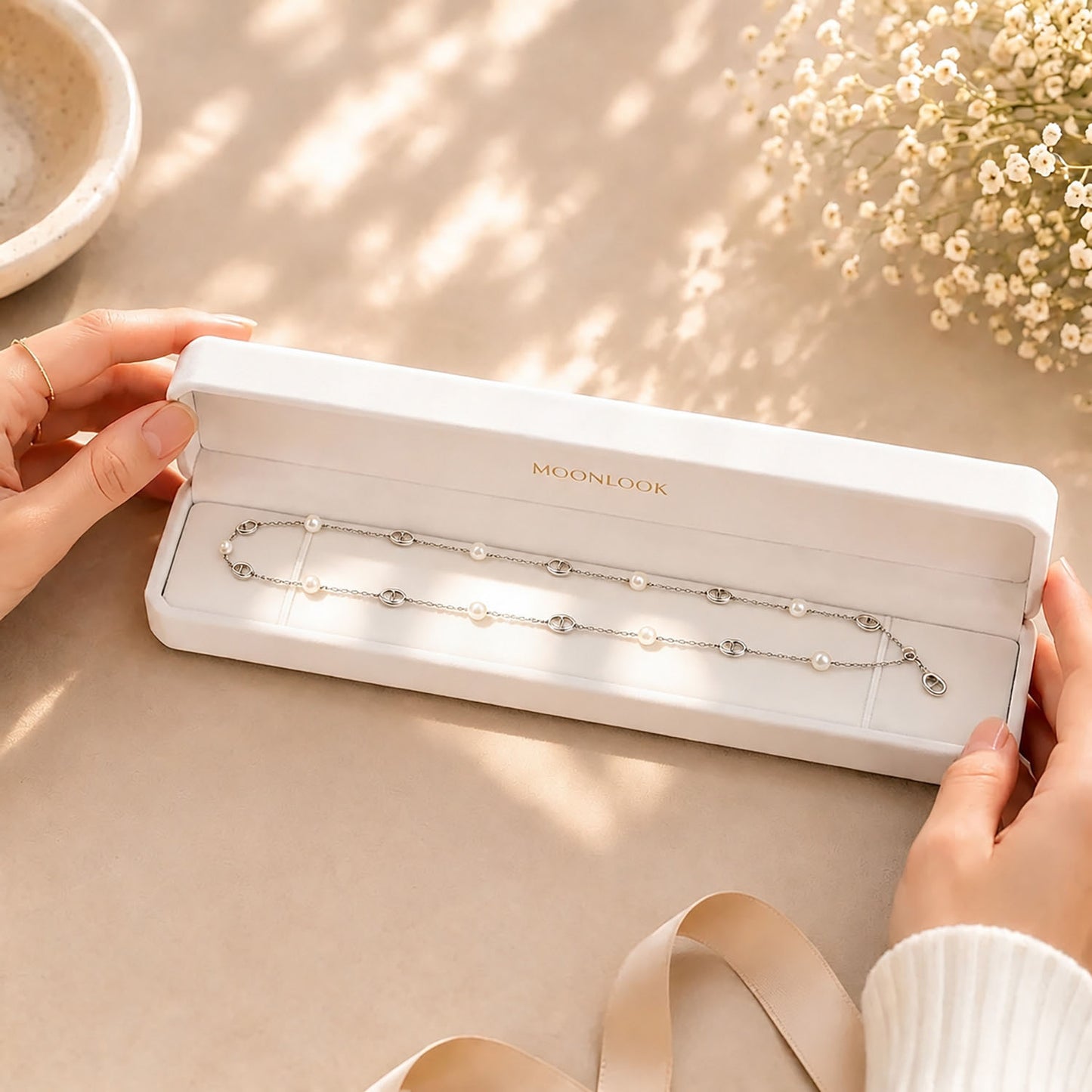 Hands opening a premium white Moonlook jewelry box revealing a delicate pearl and anchor link necklace.
