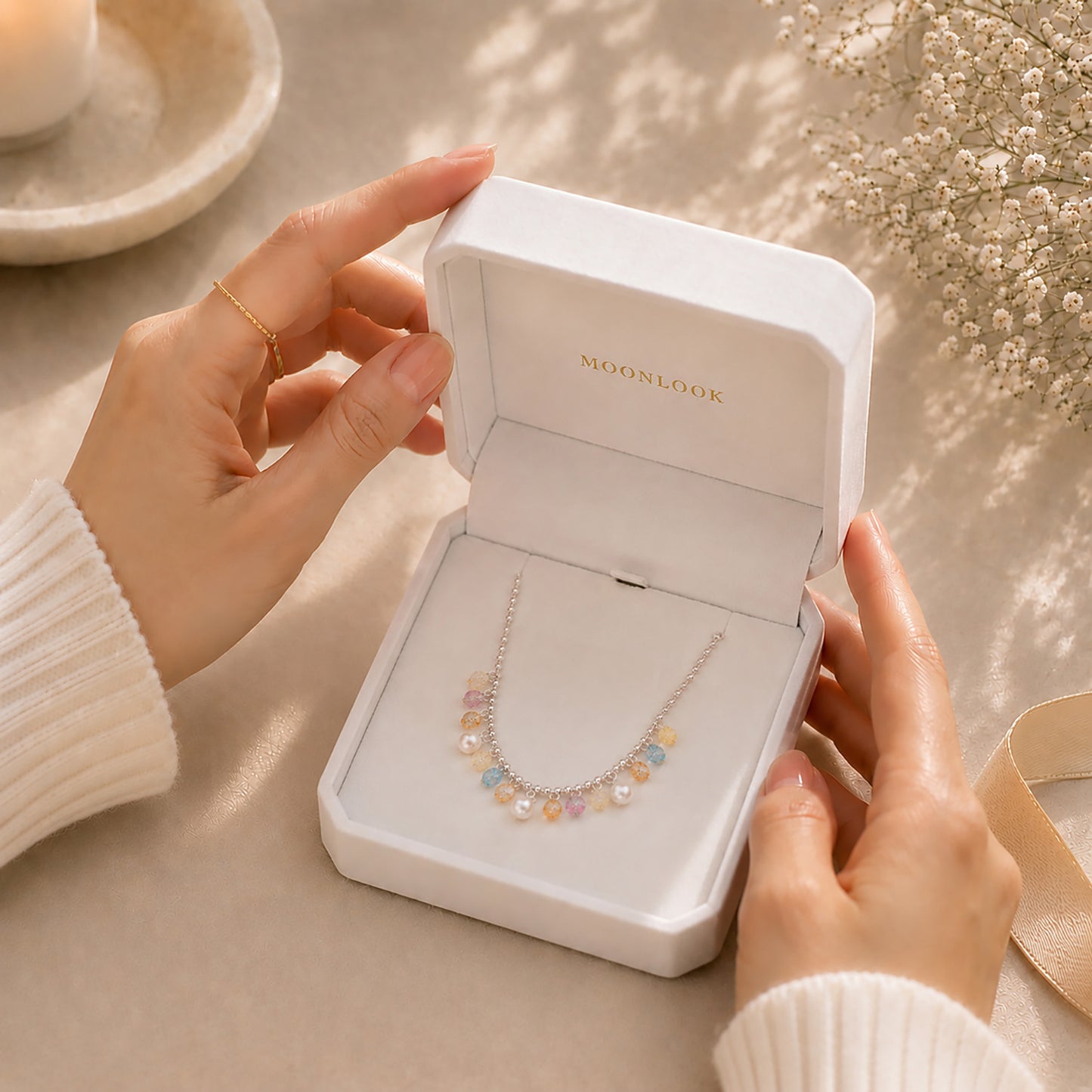 Hands opening a premium white Moonlook jewelry box revealing a sparkling rainbow zirconia necklace.