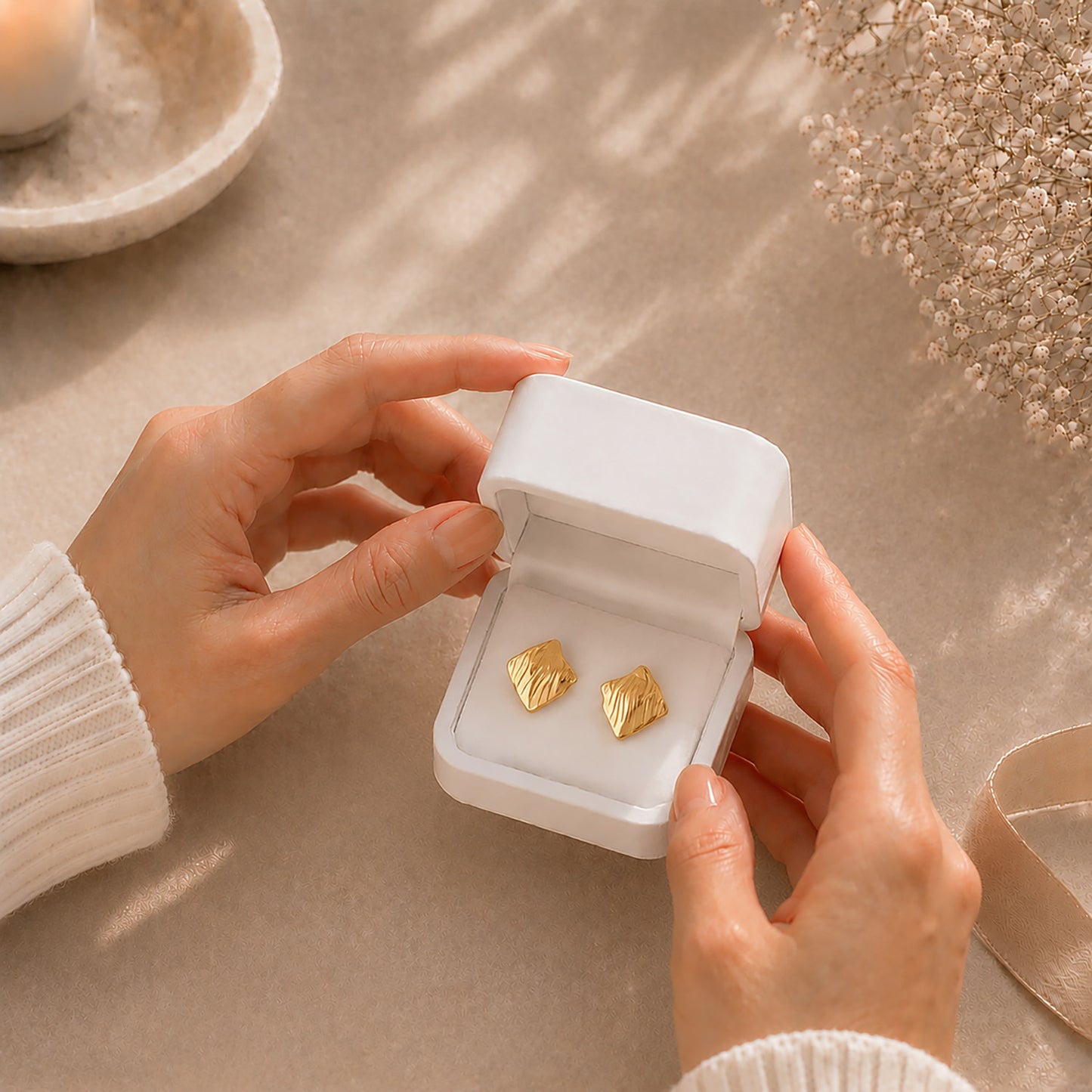 Hands gently opening a premium white Moonlook jewelry box revealing a pair of modern gold-tone crinkled stud earrings.