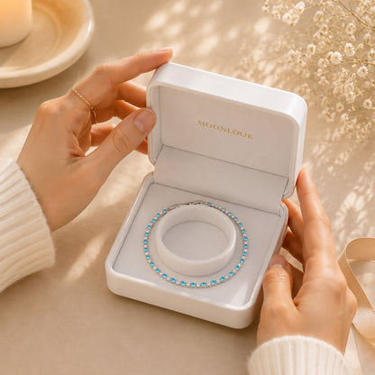 Hands opening a premium white Moonlook jewelry box revealing a delicate blue starlight tennis bracelet.