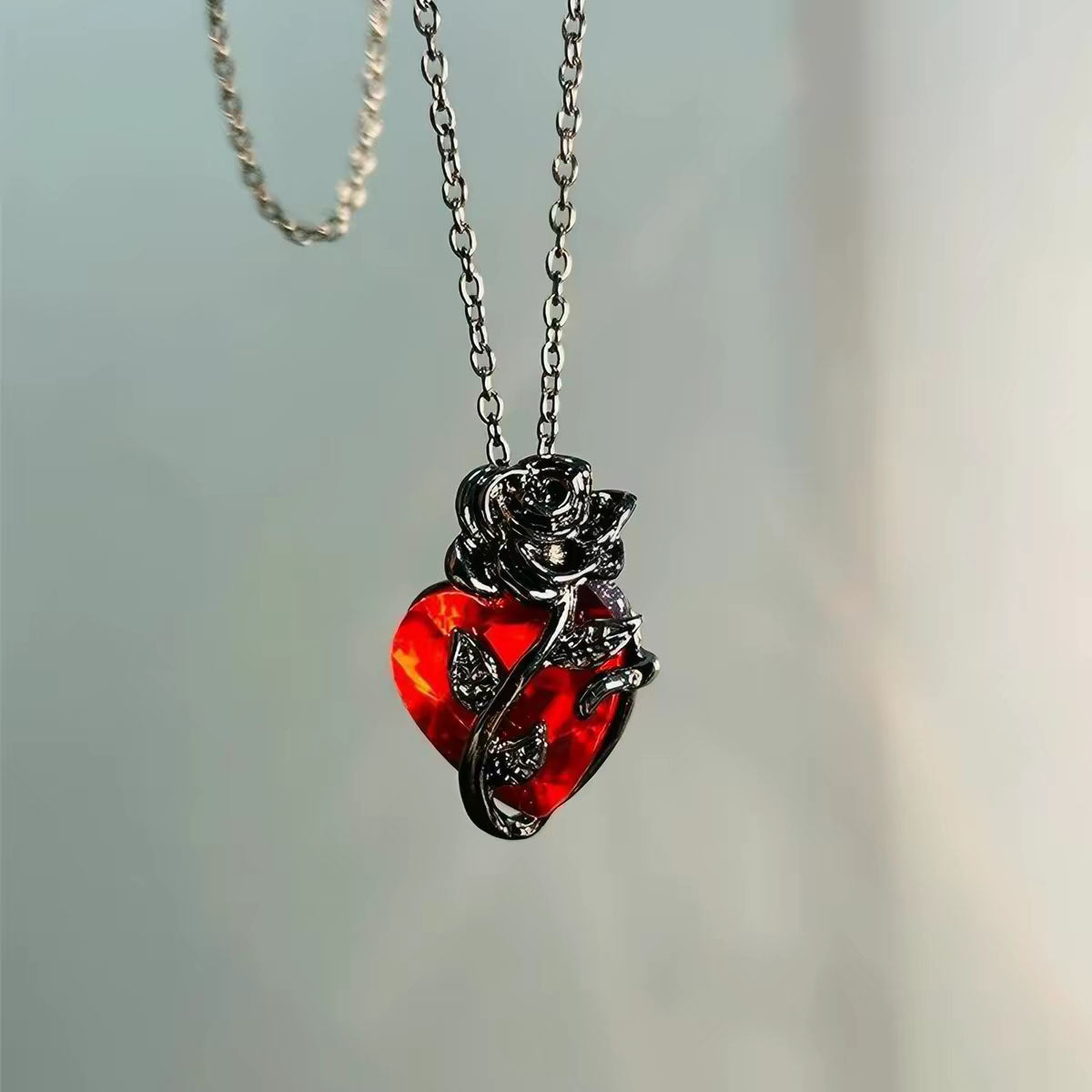 Front view of dark gunmetal black rose vine holding a sparkling ruby red crystal heart pendant