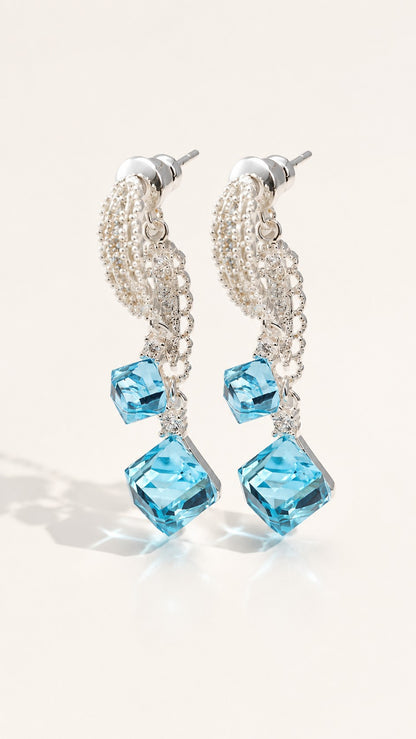 Pair of platinum plated drop earrings with double ice blue sugar cube crystals and micro-paved lace ribbon on white background