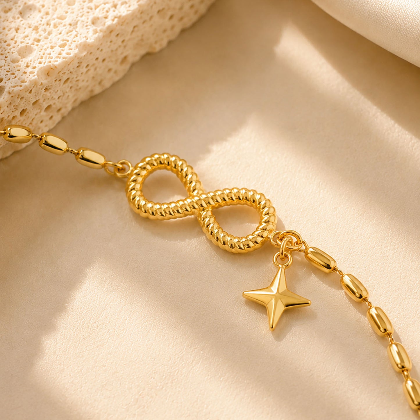 Close up detail of a textured infinity symbol and star charm on a gold-tone beaded chain.