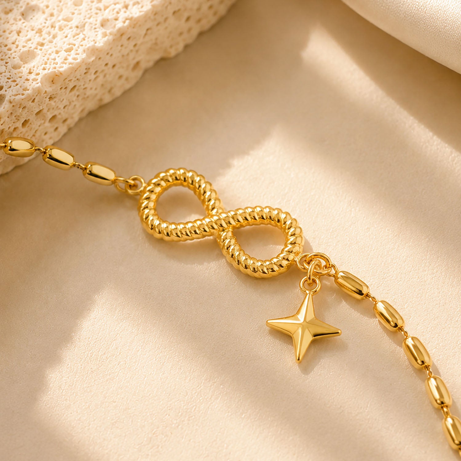 Close up detail of a textured infinity symbol and star charm on a gold-tone beaded chain.