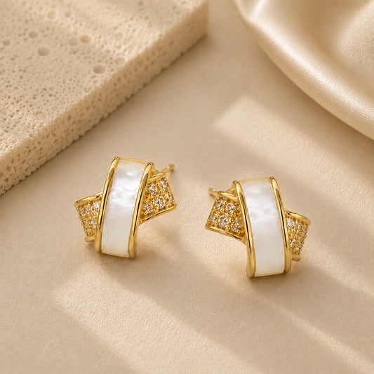 Close up of interlocking gold-tone and zirconia stud earrings on a textured surface.