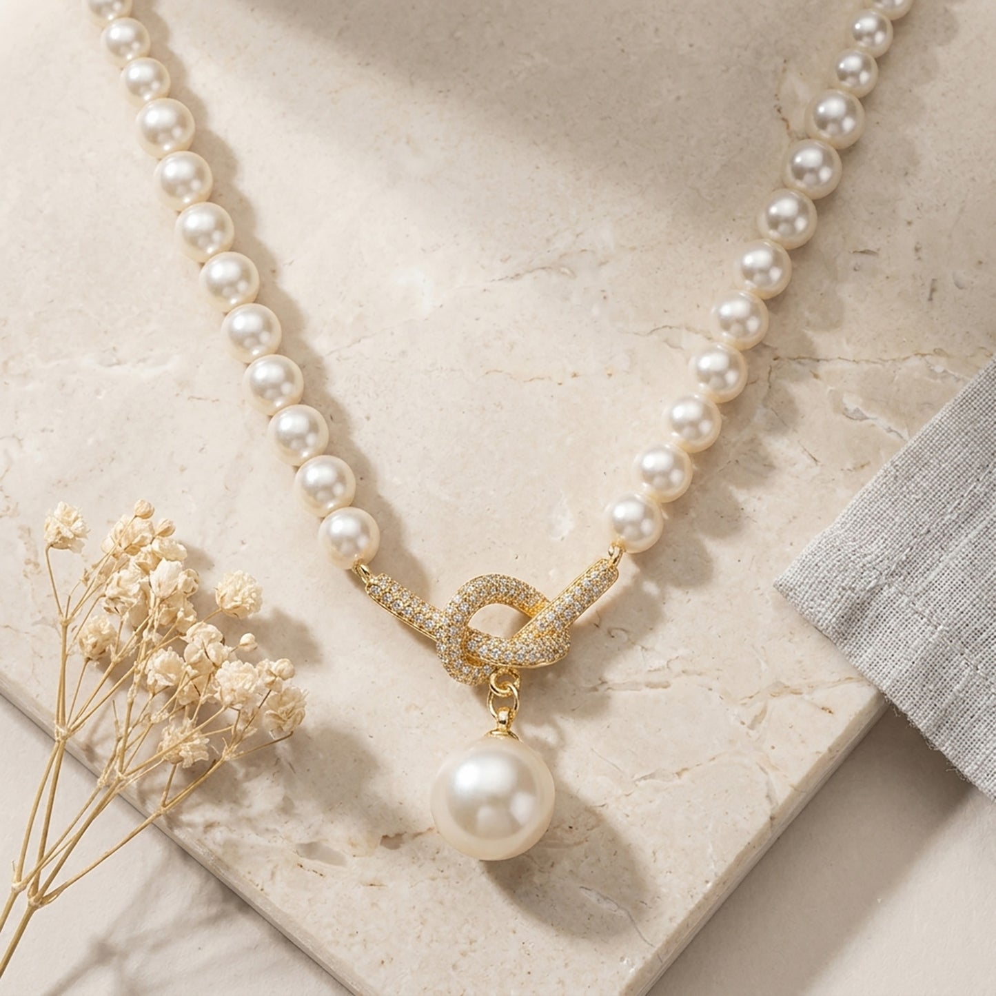 18K gold-tone knotted pearl pendant necklace laid flat on a stone surface with dried flowers.
