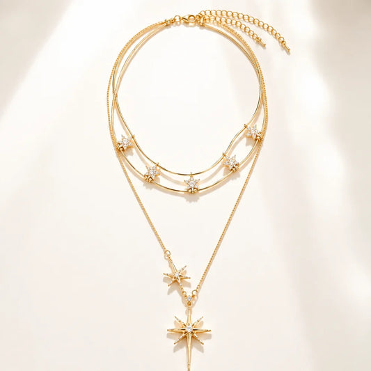 Minimalist flat lay of a complex layered gold-tone necklace featuring a double-wire choker with mini stars and a long sunburst pendant on a white background.