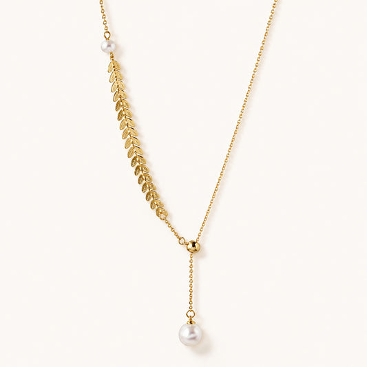 Minimalist flat lay of an elegant 18K gold-tone lariat necklace featuring a detailed leaf motif and pearl accents on a white background.