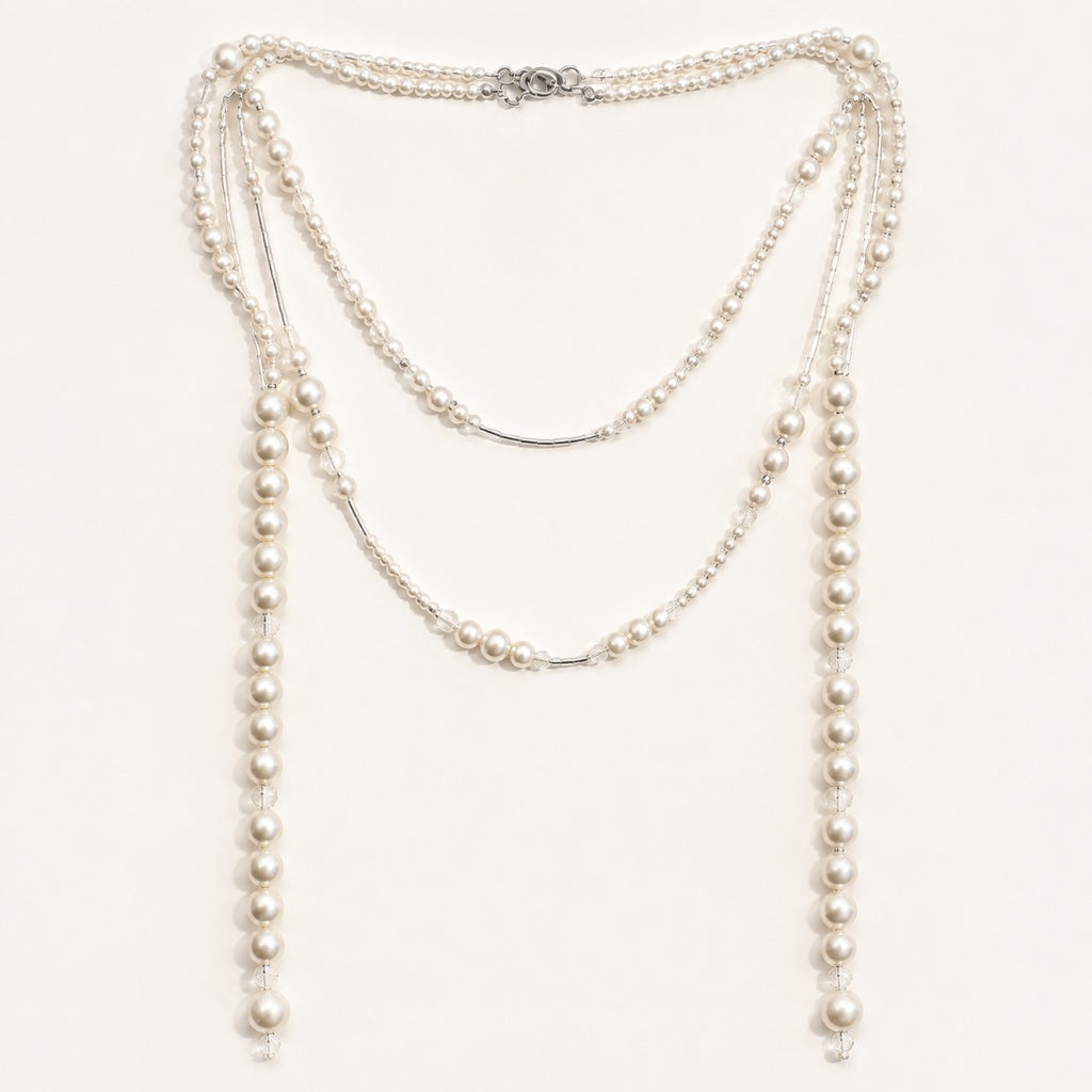 Minimalist flat lay of a long gold-tone station necklace featuring scattered simulated pearls of varying sizes on a clean white background.