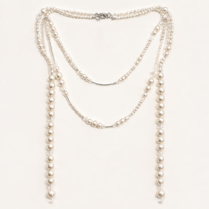 Minimalist flat lay of a long gold-tone station necklace featuring scattered simulated pearls of varying sizes on a clean white background.