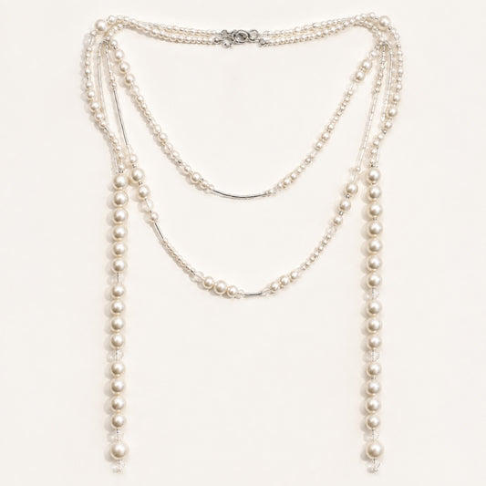 Minimalist flat lay of a long gold-tone station necklace featuring scattered simulated pearls of varying sizes on a clean white background.