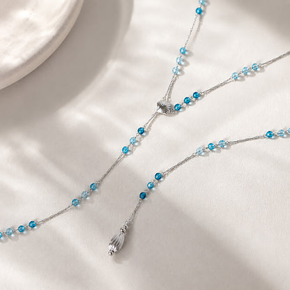 Beautiful close-up of a white gold-tone seashell lariat necklace with blue crystals resting elegantly in warm, watery sunlight.