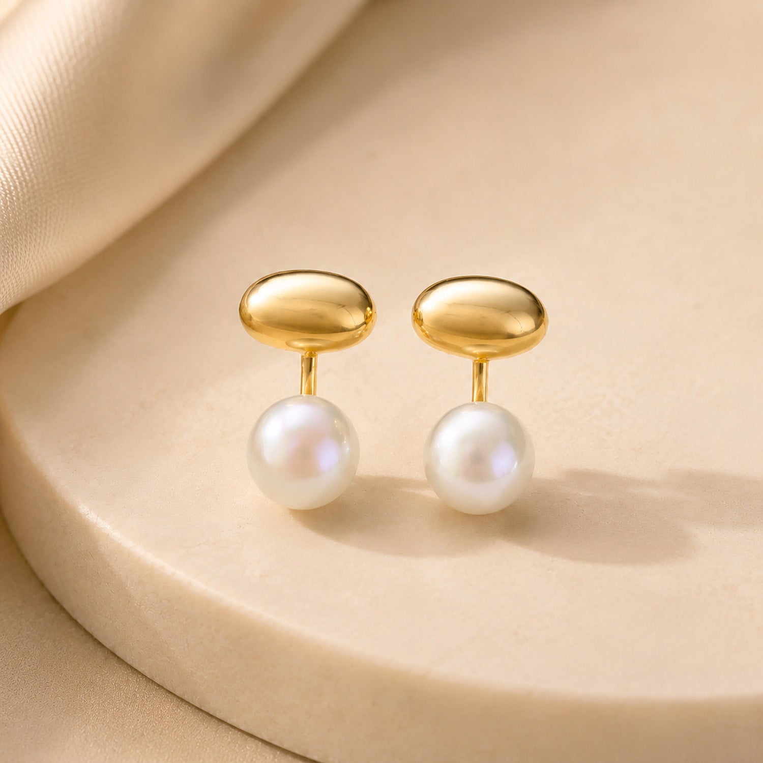 Elegant 18K gold-plated and freshwater pearl jacket earrings resting gracefully on a textured aesthetic stone surface.