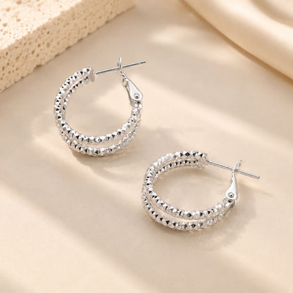 Close up of irregular white gold-tone double hoops with light-catching textures.