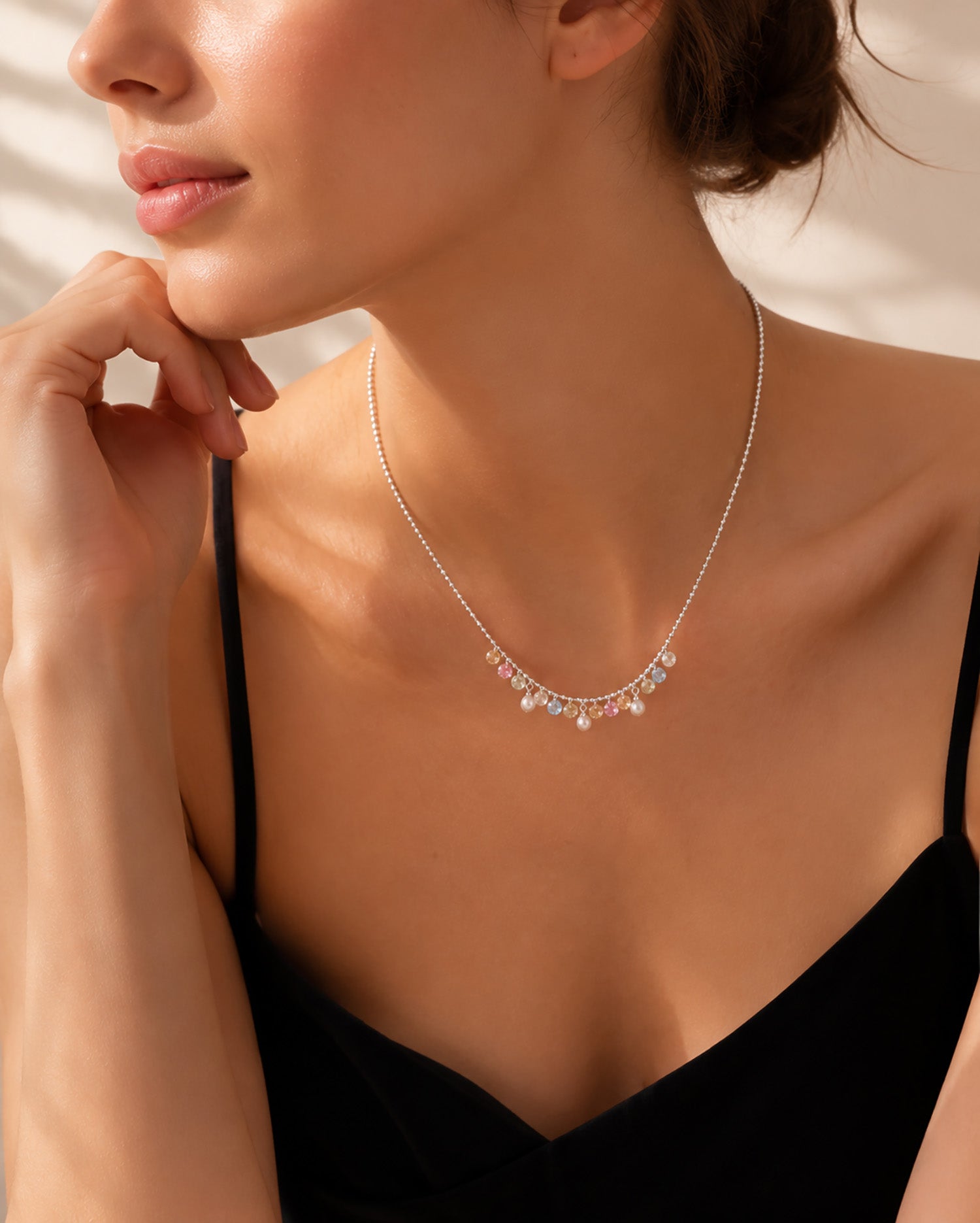 Elegant woman in a black slip top wearing a colorful zirconia fringe collarbone necklace.