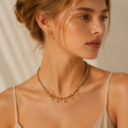 Close-up profile of a woman styling a delicate gold-tone beaded necklace with colorful stones.