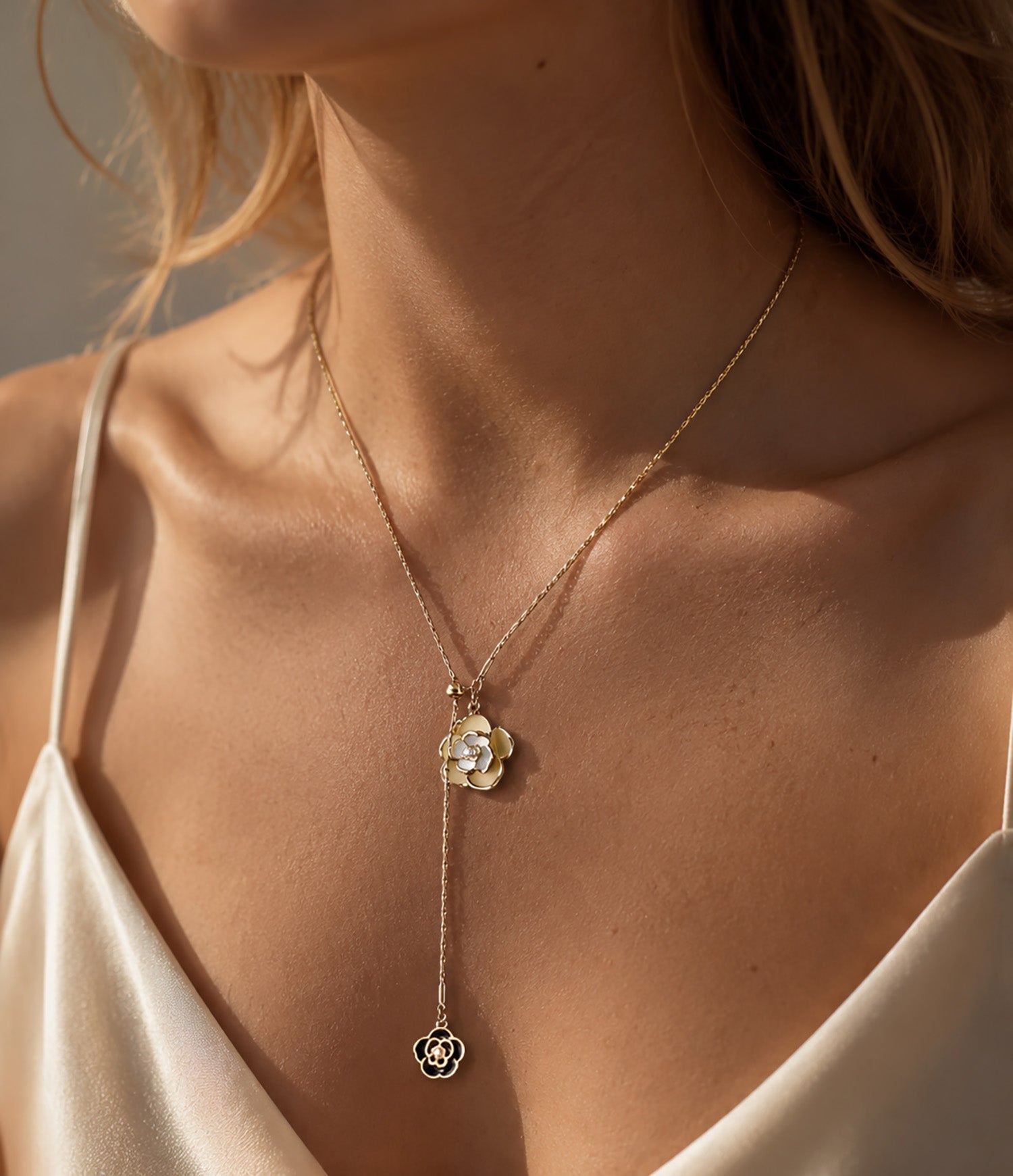 Close-up of a woman's décolletage styling a classic monochrome camellia Y-necklace with a silk dress.