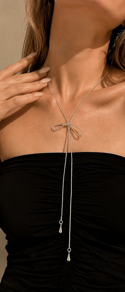Close-up of a modern woman's décolletage showcasing a delicate silver-tone adjustable bow necklace with liquid-like snake chains.