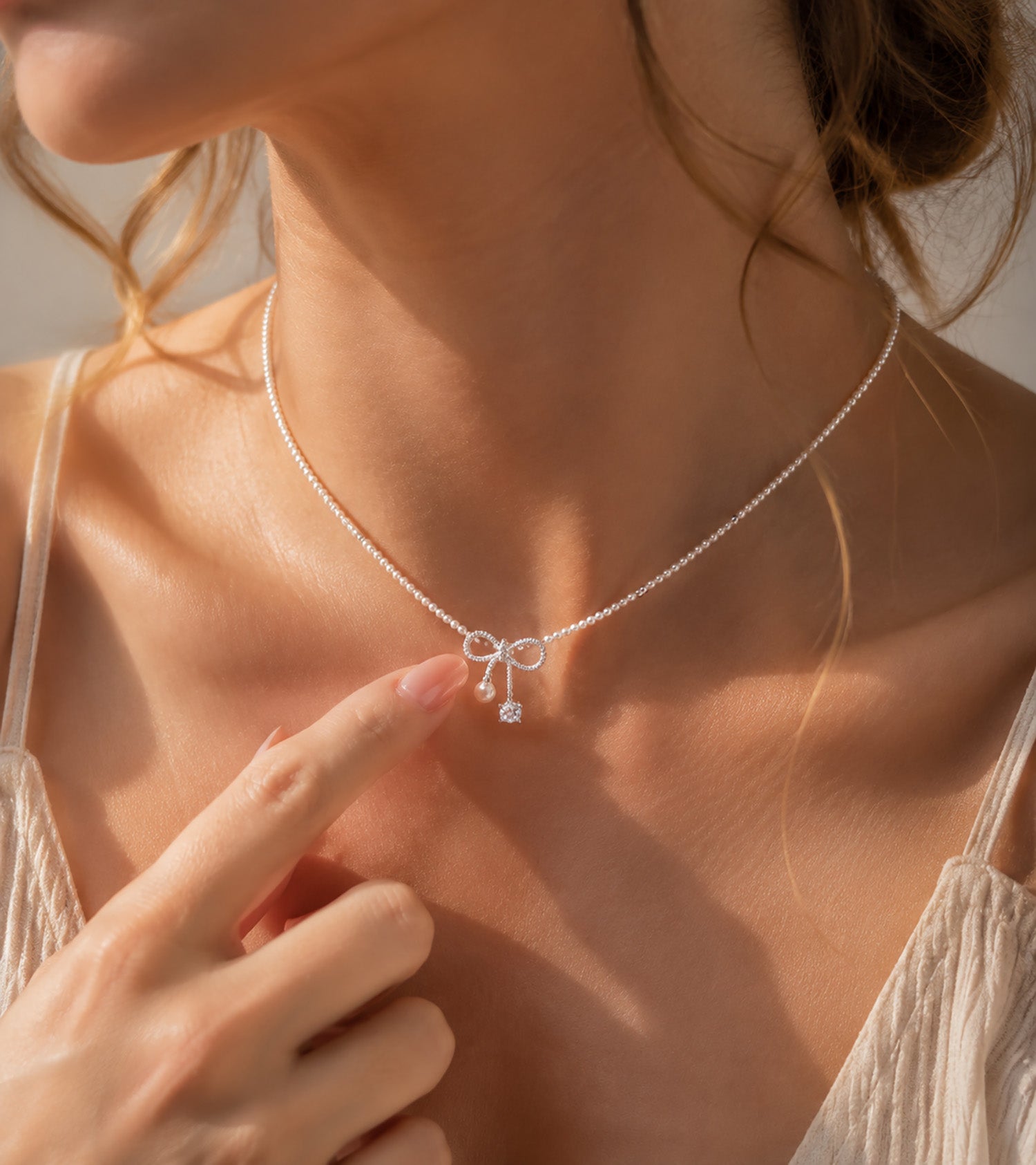 Close up of a woman gently touching her elegant pearl and zirconia bow necklace.
