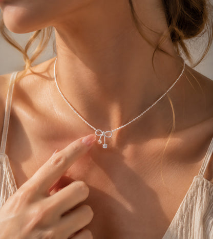 Close up of a woman gently touching her elegant pearl and zirconia bow necklace.