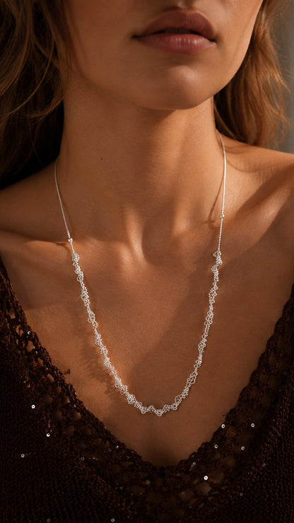 Sunlit close-up of model wearing multi-way silver lace necklace styled with long Y-chain drop
