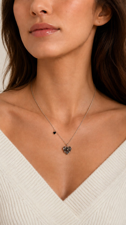 Front view close up of model wearing silver chain necklace with black crystal heart pendant and white sweater