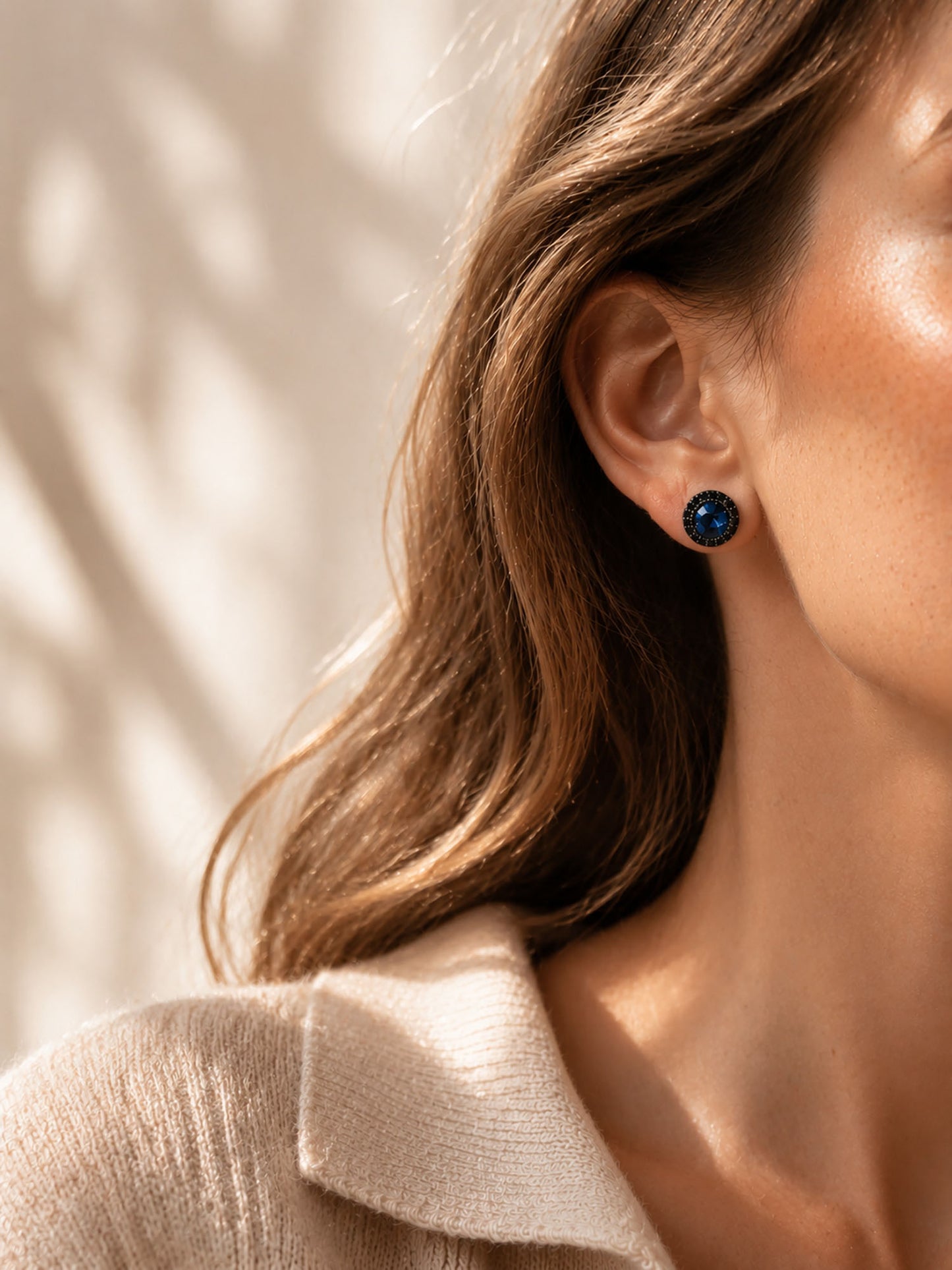 Elegant woman wearing bold black zirconia halo stud earrings with a cozy beige knit sweater.