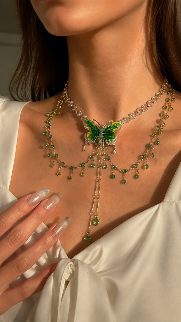 Elegant modern woman wearing a crisp white silk top, styling a breathtaking 18K gold-tone layered necklace featuring a vibrant green butterfly pendant and crystal accents resting perfectly on the collarbone.