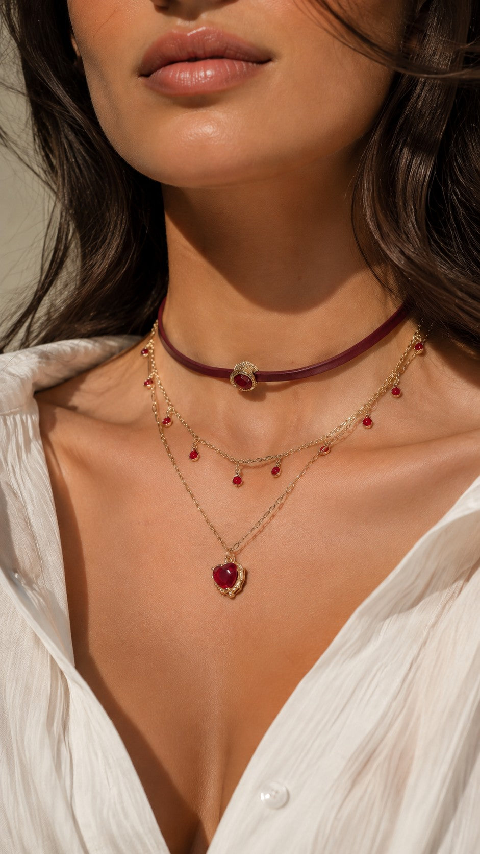 Close up of model wearing burgundy leather choker and gold layered necklace with ruby red heart pendant