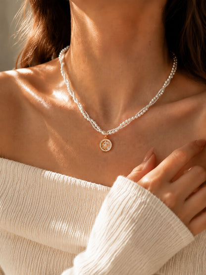 Elegant woman wearing a gold-tone compass pendant and double-layer twisted pearl necklace beautifully illuminated in warm sunlight.