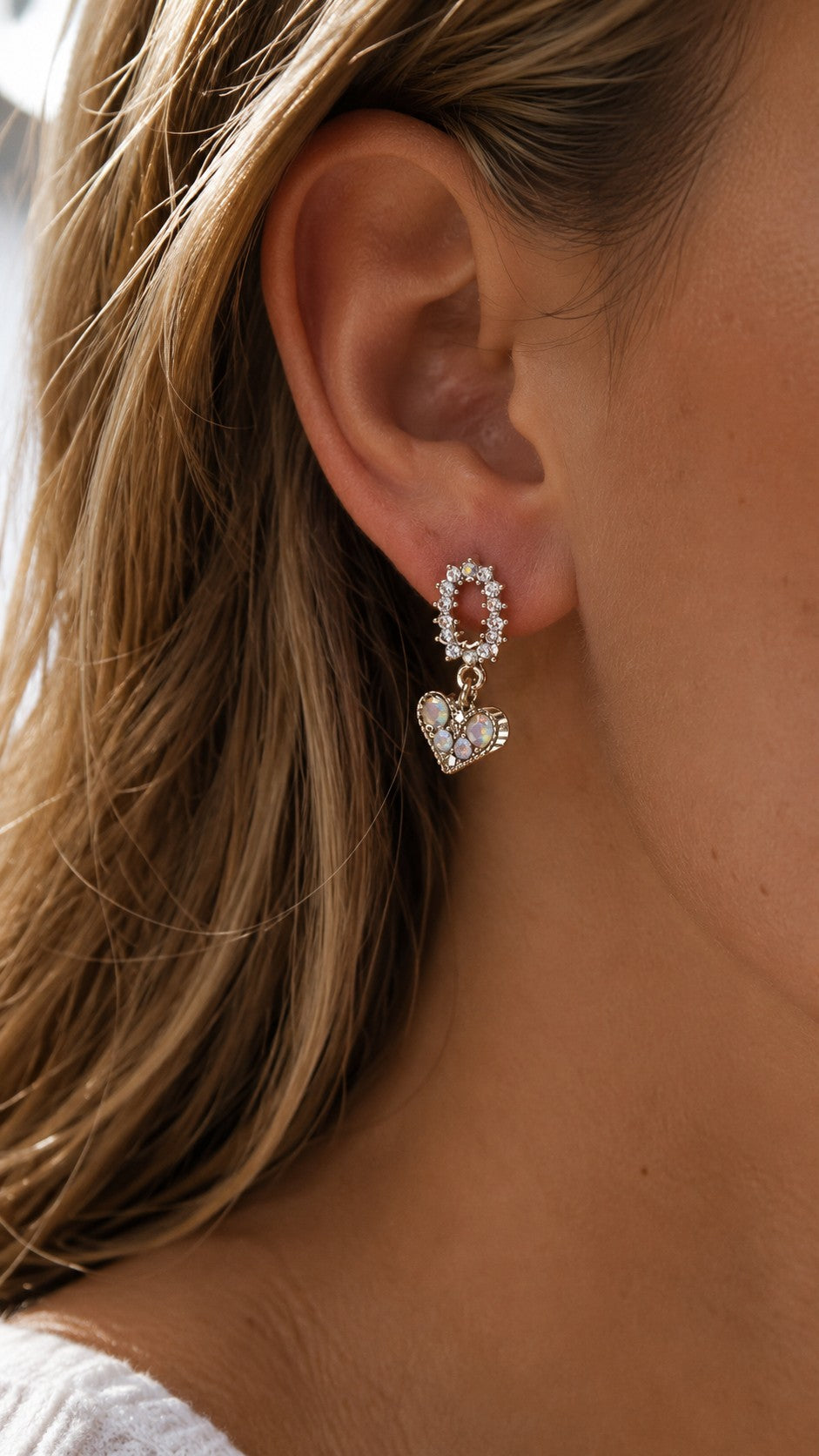 Side profile close-up of model wearing dainty gold iridescent CZ heart drop earrings