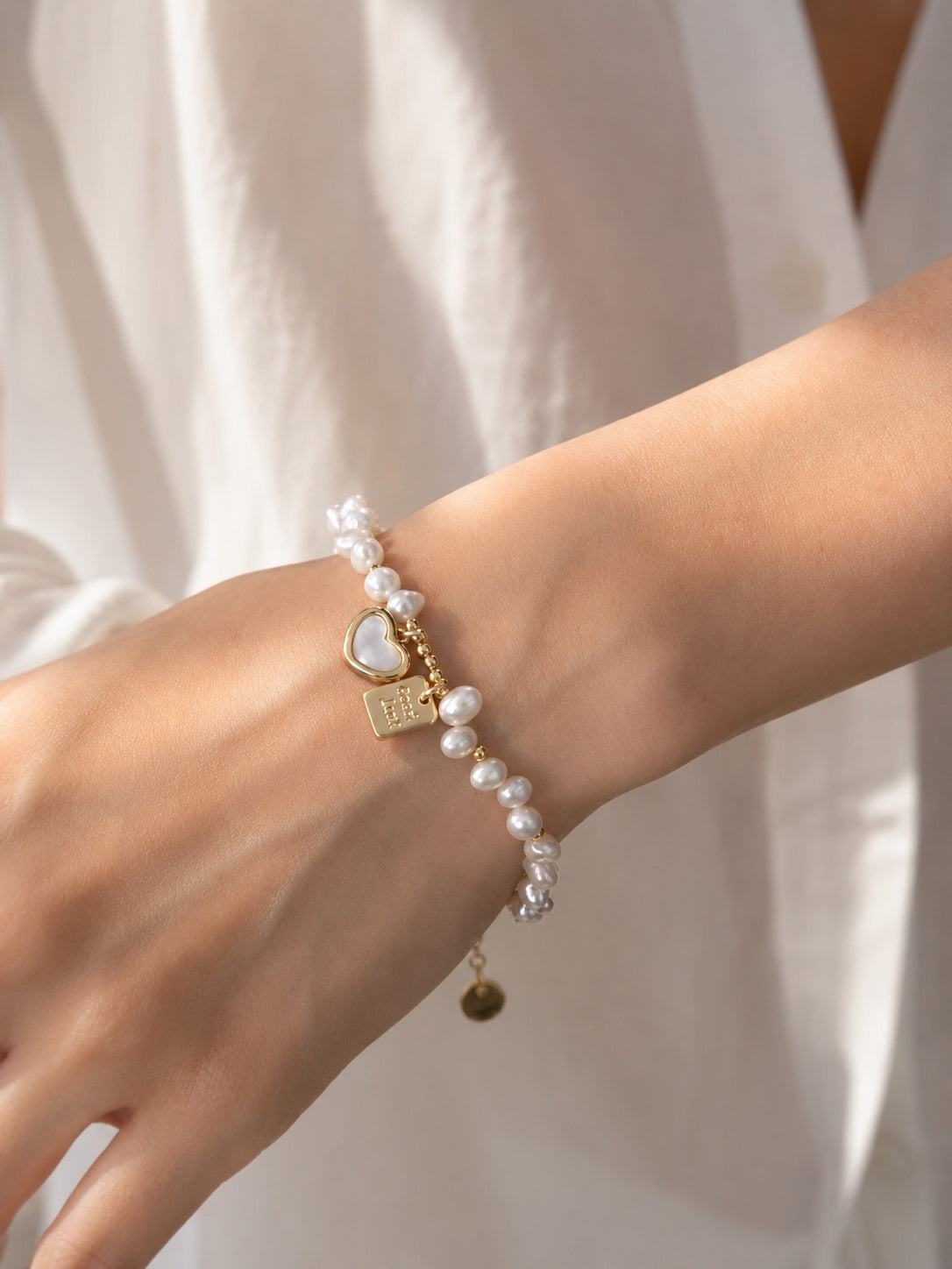 Model wearing white linen shirt showcasing real freshwater pearl heart charm bracelet on wrist