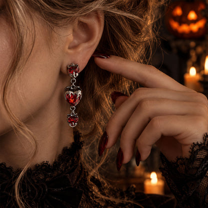 Close-up of model wearing gothic bleeding red heart drop earrings with black lace dress