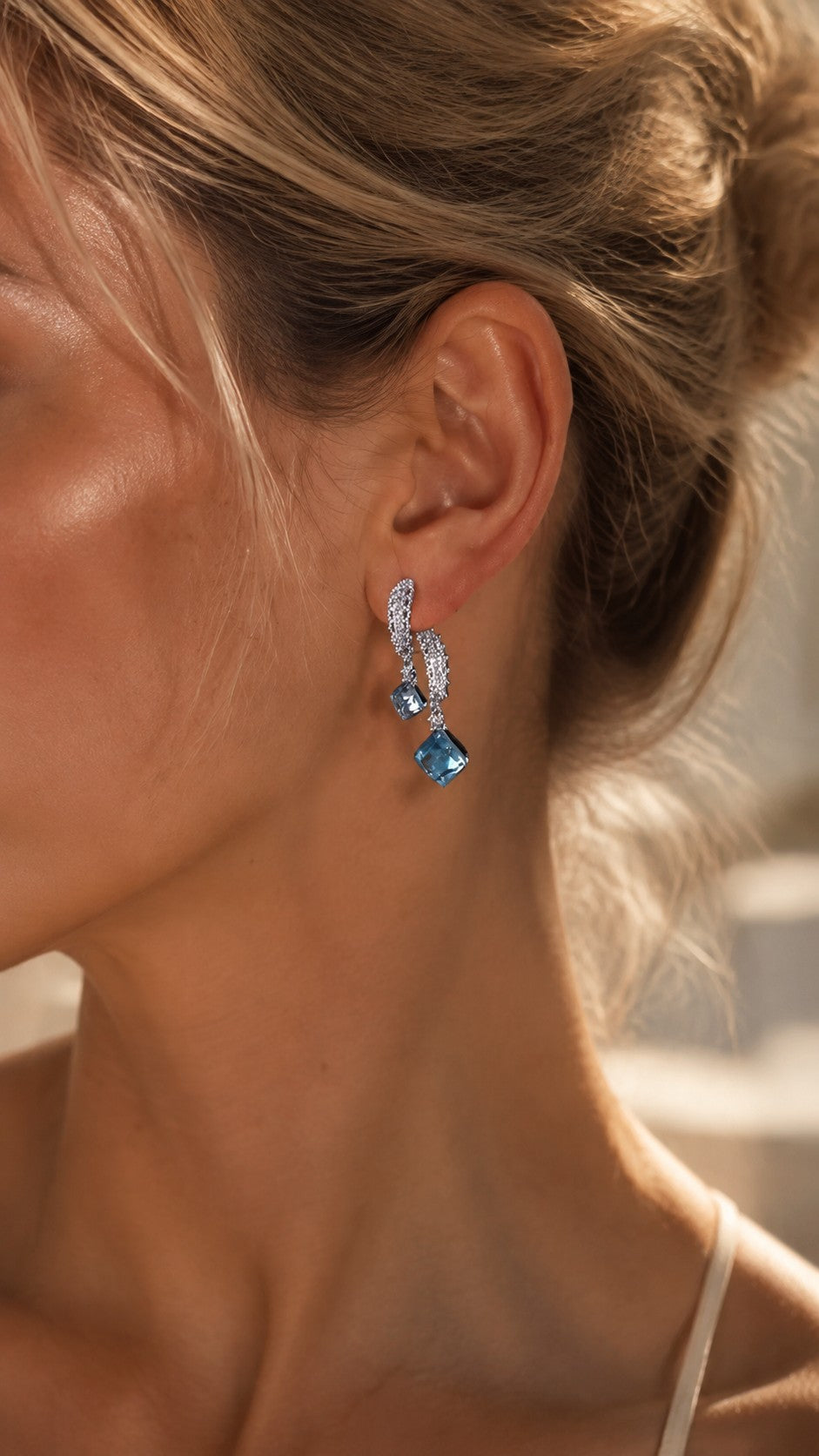 Blonde model with elegant updo hairstyle wearing ice blue sugar cube crystal drop dangle earrings under warm sunlight