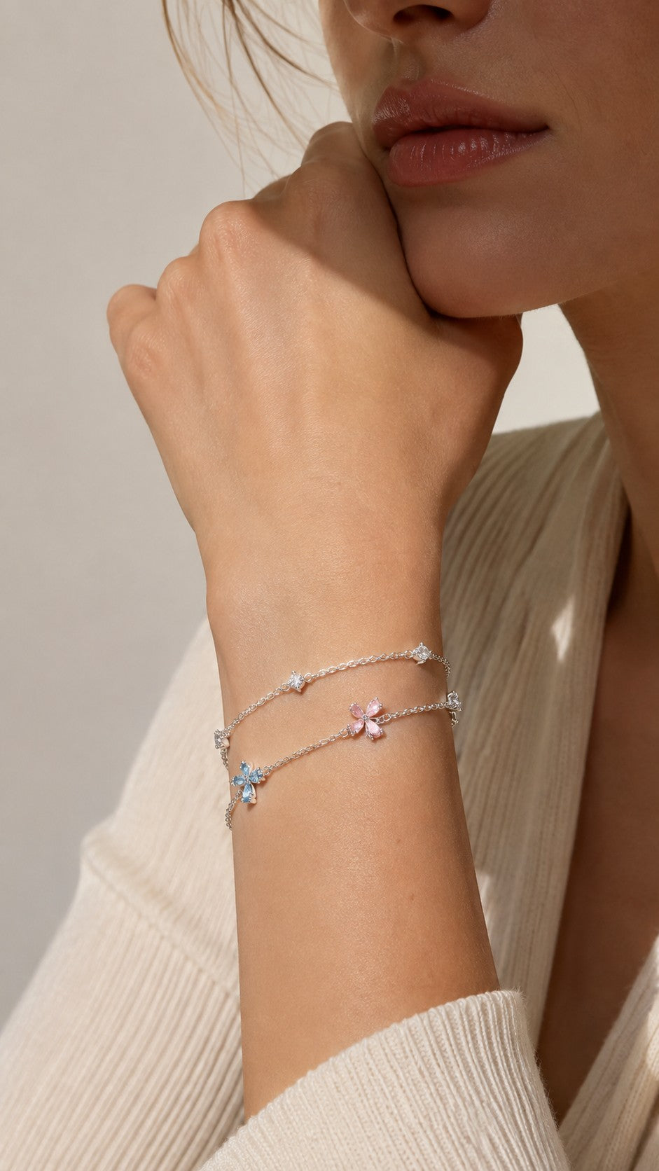 Close up of model rest hand wearing dainty pastel four-leaf flower double strand silver bracelet with cream sweater