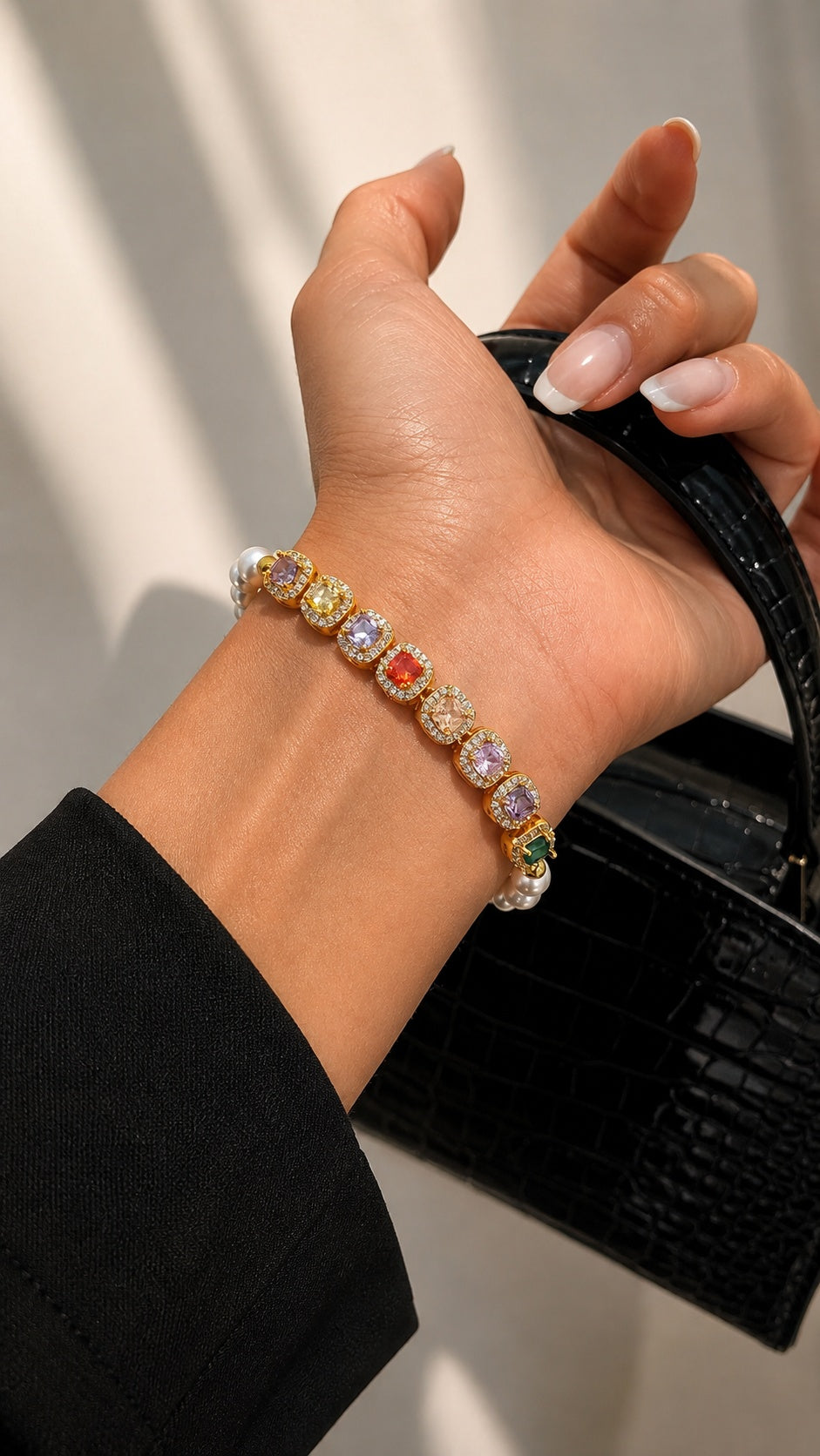 Close up of model wearing rainbow candy crystal pearl bracelet on wrist holding a black leather bag