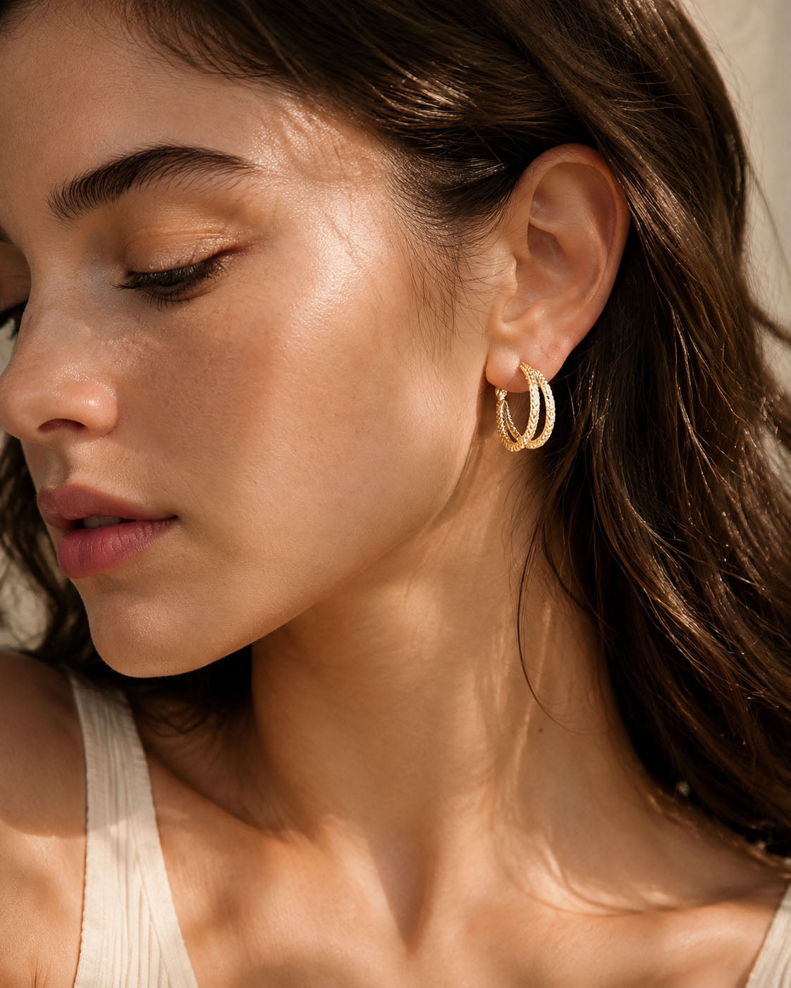 Close-up of an elegant woman wearing vintage textured double hoop earrings in a radiant gold-tone, illuminated by soft sunlight.