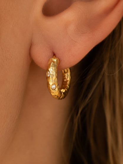 Macro close-up of a modern woman styling 16mm chunky gold-tone hoop earrings with an organic hammered texture and zirconia accents.